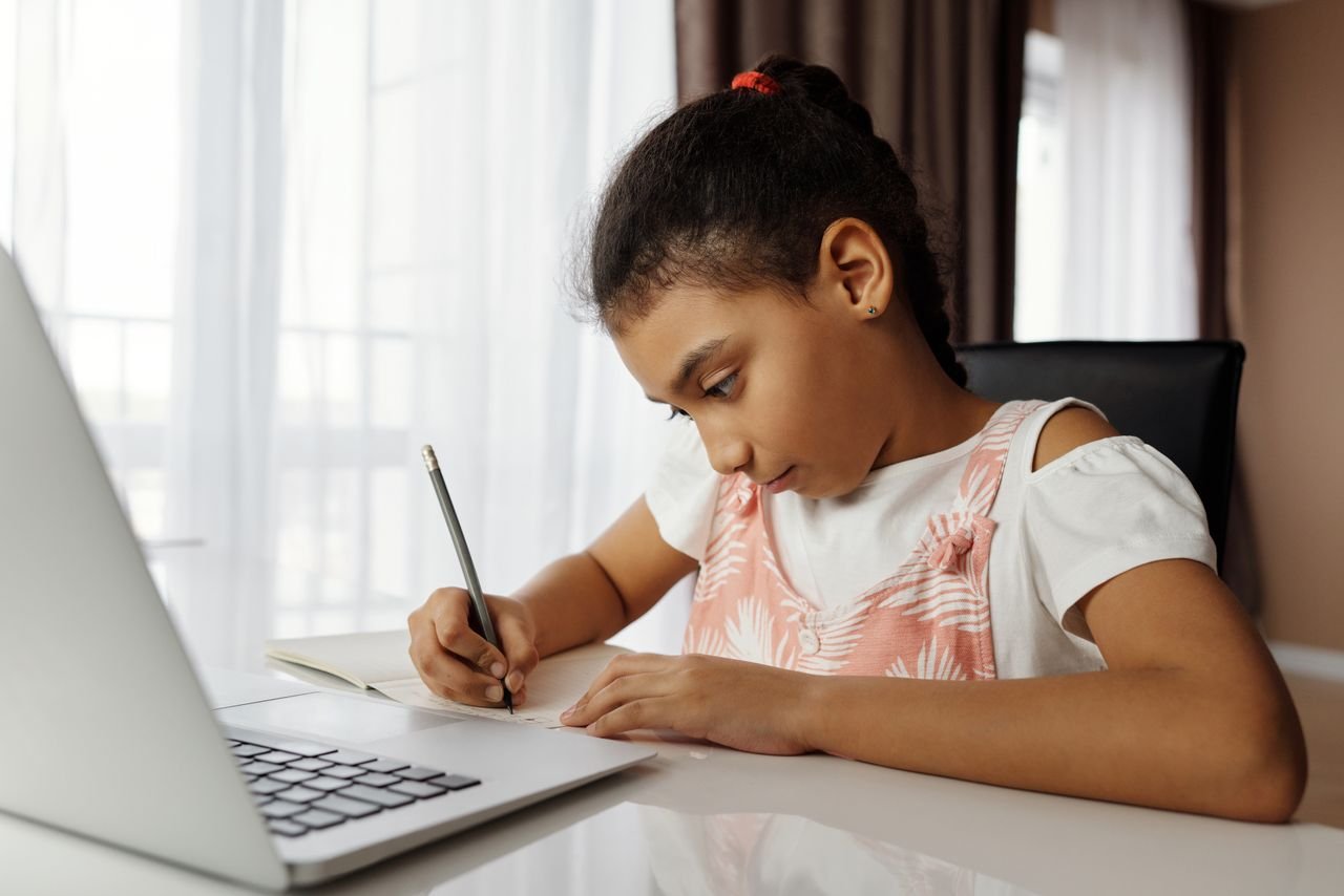 Young girl focusing on homework, using a laptop indoors. Ideal for education themes.